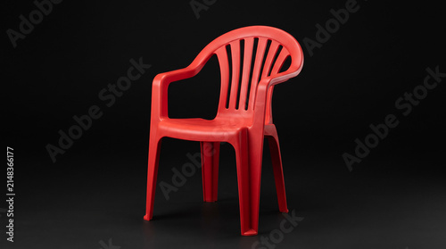 Bright red plastic outdoor chair isolated on a black background.