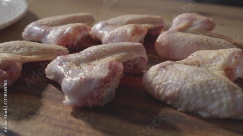 Camera Gliding Along Raw Chicken Wings as Seasoning Falls