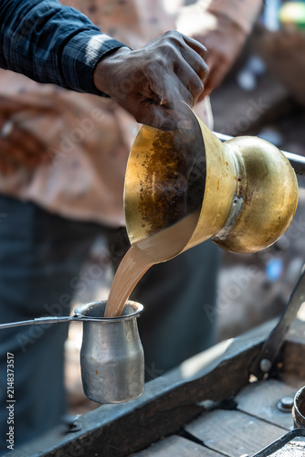 India. Rajasthan. Bundi. Preparing chai (Indian tea). Close-up of a street vendor pouring steaming chai, prepared in a traditional brass teapot