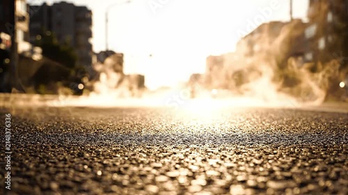 Steam rising from asphalt road on sunny day. Urban street surface with vapor mist at sunset. Cinematic view of city pavement with heat haze in golden light.