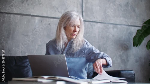 Senior Caucasian woman working on laptop and looking away while thinking at home office. Mature female reviewing documents and planning tasks at desk. Remote work. Business lifestyle.