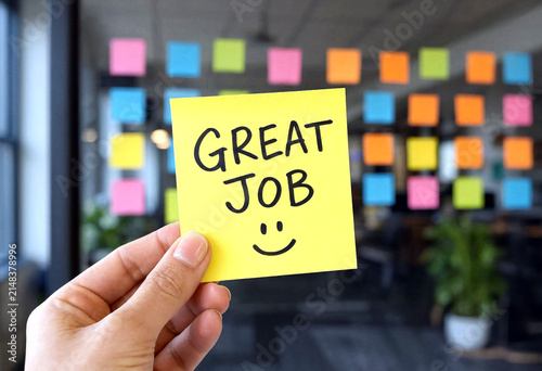 Happy person holding a yellow sticky note with great job written and smiley face in office setting