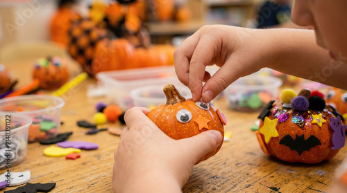 Children halloween pumpkin decorating craft classroom closeup hand autumn festive art activity with googly eye and foam shape small pumpkin wooden table, cheerful holiday workshop for kid