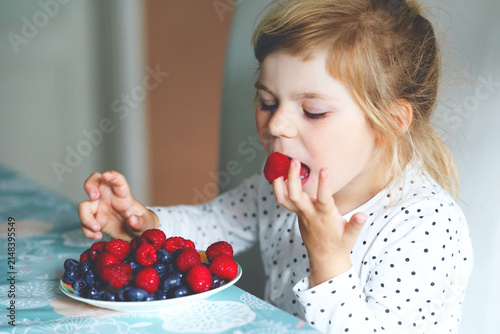 Konstfotografi Cute little preschool girl eating fresh raspberries and blueberries