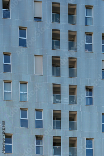 Under even daylight, blue tones settle over a minimal apartment facade, where repetition organizes windows and balconies across Nordbahnviertel, Vienna, Austria.