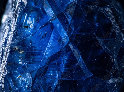 Raw sapphire fills the frame with vivid deep electric blue in dramatic sidelight — the most precious blue stone as ultimate fine art. Ideal for luxury, jewelry, and premium design backgrounds.
