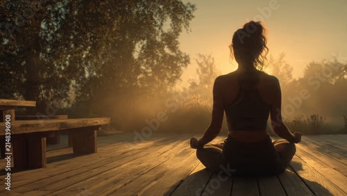 A young woman practices meditation on a wooden deck during sunrise enveloped in soft golden light promoting emotional wellness and tranquility