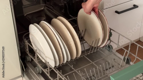 Close up of woman hands loading dirty ceramic plates into a modern dishwasher. Housework, kitchen routine and smart home appliances concept.