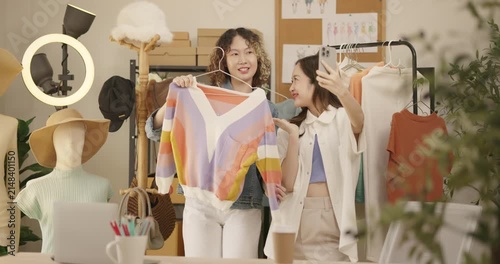 Asian woman influencer live streams a fashion product showcase from studio. Two female SME Online store business owner selling clothes on social media. entrepreneur, e-commerce, side hustle concept.