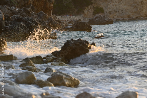 White sea foam washing over coastal rocks and stones under warm golden sunset light background