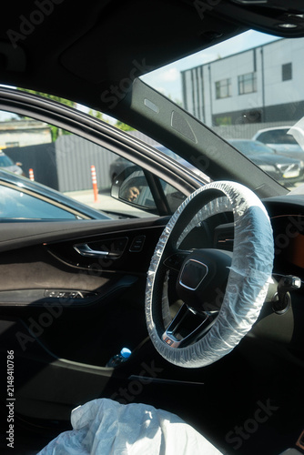 Plastic cover wraps steering wheel rim inside car cabin with door open. Disposable barrier protects seat area supporting clean service handoff