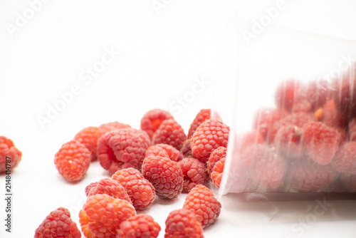 Obraz na plátně Ripe raspberries tumbling from their container create a vibrant and inviting sce