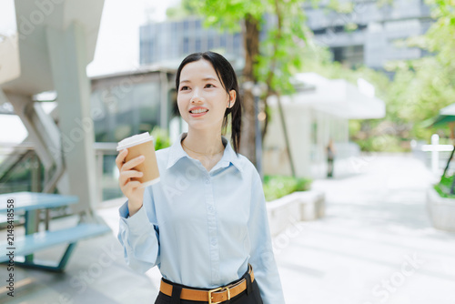 Smiling young businesswoman holding a takeaway coffee cup outdoors near a modern office, representing coffee break, professional lifestyle, workday routine, career, and workplace wellbeing.