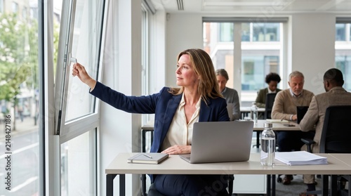 Office employee woman opens nearby window during sudden hot flash, creating clear menopause workplace image focused on discreet cooling, comfort and professional dignity today.