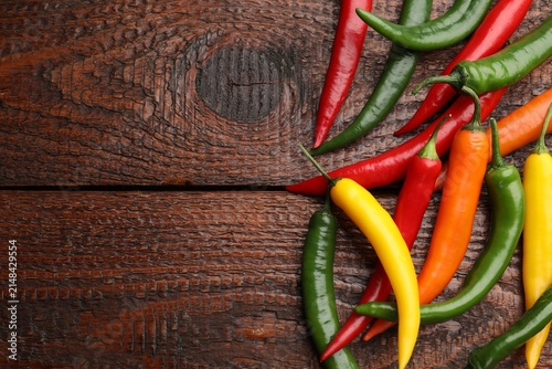 Фотография Fresh colorful chili peppers on wooden table, flat lay