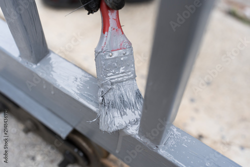 Hand holding a brush, applying paint to a metal fence improvement project involves fence restoration and exterior upkeep with fresh color.