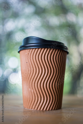 A kraft paper coffee cup with a black plastic lid for hot drink on wood table