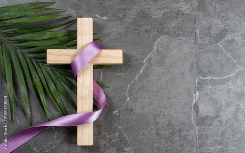Wooden cross wrapped in purple ribbon with palm leaf on gray stone