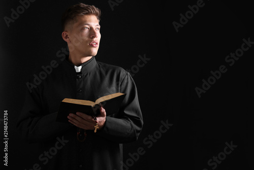 Priest with Holy Bible on black background. Space for text