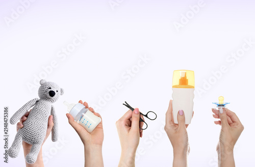 Women holding toy bear, feeding bottle and other baby stuff on light background, set
