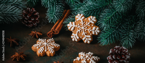 Gingerbread snowflakes with Christmas decorations and spices on a dark rustic background, selective focus, panoramic banner