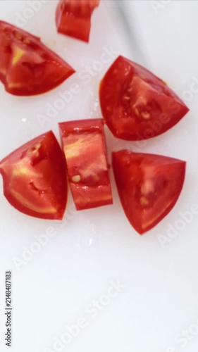 Fresh tomato cutting close up on white kitchen board. Chef hands in blue gloves mince red vegetable with big iron knife. Cooking, preparing ingredients in professional restaurant. Top down view