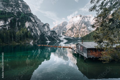 Braies, Italy - 06 June 2024: View of the iconic wooden boathouse on the emerald waters of Lago di Braies with a line of rowing boats and the majestic Seekofel mountain peak.