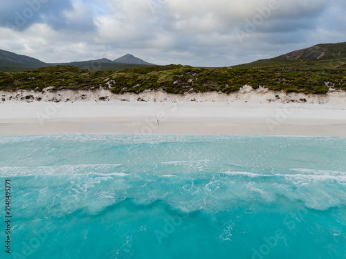 Aerial view of Hellfire Bay with turquoise waves washing onto white sand and a person walking along the shore in Cape Le Grand National Park, Western Australia, Australia.