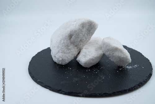 Foto Close-up of white rock salt crystals and chunks (Artymovske mineral) on a black slate plate