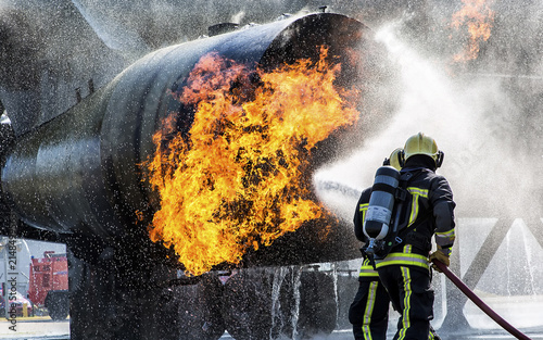 View of firefighters using a hose to extinguish a large fire erupting from a metal training tank at a fire station in Badhoevedorp, Noord-Holland, Netherlands.