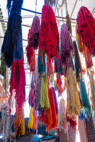 skeins of colorful dyed wool yarn hanging overhead to dry inside traditional dyers market workshop at historic Medina souk in Marrakech Morocco