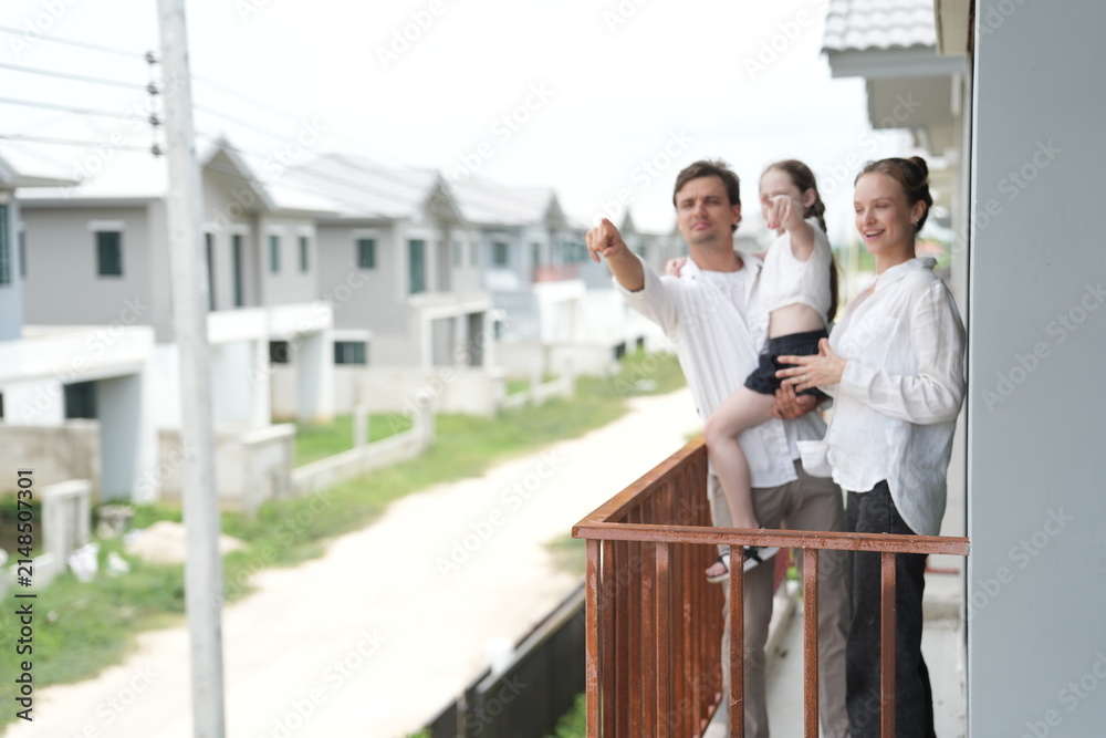 Obraz premium Caucasian family of three embracing enjoy the view of the growing suburb from their balcony standing on the terrace of a newly built suburban home, shallow depth of field