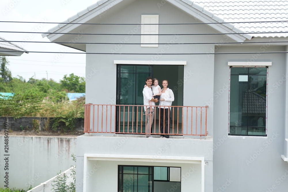 Obraz premium Young parents holding their child enjoy the view of the growing suburb from their balcony on the upper balcony of their new home above the neighborhood, candid real moment