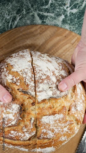 A baker splits two halves of freshly baked wheat sourdough bread over a board, showcasing the open crumb structure. Close-up highlights the golden crust and airy texture. Vertical video.