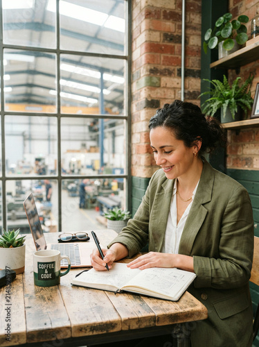 Businesswoman writing in a notebook at a factory office desk