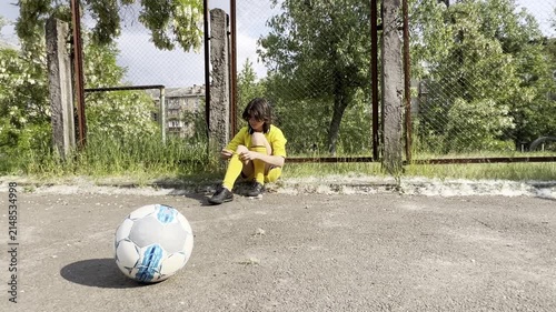Teen boy sitting on outdoor court after football training adjusting socks and resting fatigue recovery effort and youth sport lifestyle concept. High quality FullHD footage