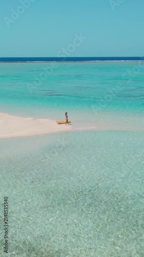 Woman walks gracefully on a white sand beach in the maldives with a yellow kayak, surrounded by turquoise waters and clear blue skies, creating a serene tropical paradise