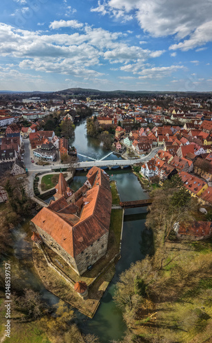 Aerial view of Wenzelschloss castle surrounded by the river Pegnitz with historic town rooftops and a bridge in the background in Lauf an der Pegnitz, Bavaria, Germany.