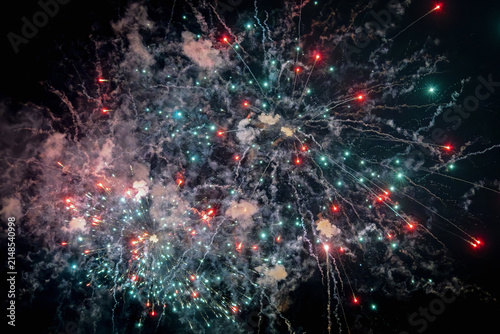 Red and teal/cyan fireworks display bursting in the night sky.