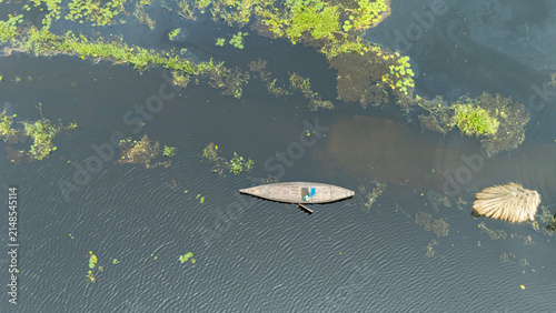 Flooded monsoon waters cover Bortir Bil, North 24 Parganas, West Bengal, India. A lone boat crosses the wetland as farmers harvest jute, fishermen work, and red water lilies bloom across the landscape