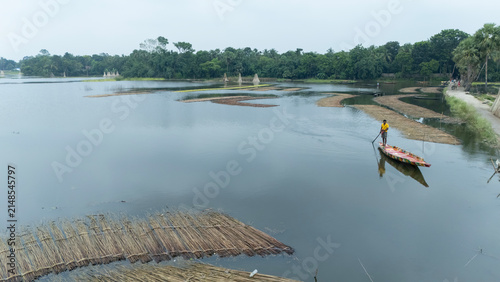 A man rows a small wooden boat across the monsoon-flooded waters of Bortir Bil, North 24 Parganas, West Bengal, India. This seasonal wetland, known for jute harvesting and red water lilies.