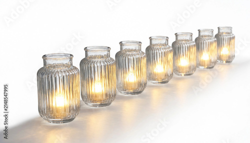 Row of decorative ribbed glass candle holders with warm glowing flames placed on a white surface interior lighting celebration atmosphere translucent ambiance tabletop centerpiece peaceful