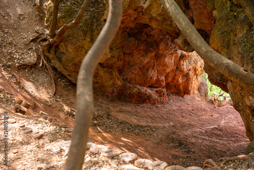Natural stone cave entrance with tree roots and red soil along a forest hiking trail in Budapest Hungary on a sunny day
