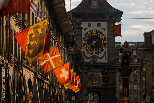 Medieval Zytglogge Clock Tower with Swiss Flags along Historic Old Town Street in Bern Switzerland during Sunset Golden Hour