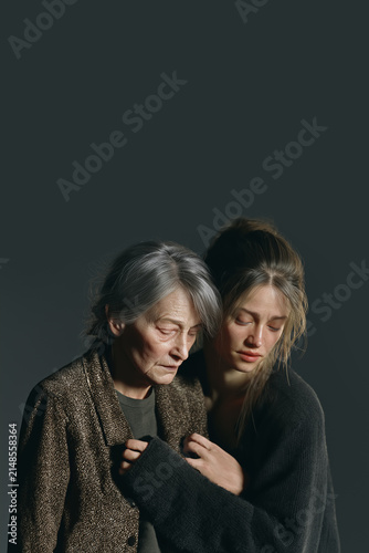 Elderly Woman Embraced by Younger Woman in Moody Dark Studio, Capturing Generational Bond, Comfort and Quiet Emotional Connection with Copy Space. Aspect Ratio Vertical 2:3