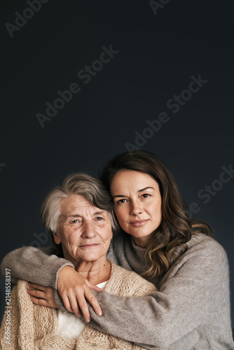 Elderly Woman and Younger Woman Embracing in Soft Sweaters Isolated Against Black Background , Symbolizing Love, Family Bond, Generational Connection and Emotional Support with Copy Space. Aspect 2:3