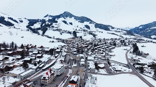 Aerial view of the snow-covered village of Chateau-d'Oex nestled in the Swiss Alps with surrounding mountains and winding roads in Chateau-d'Oex, Vaud, Switzerland.