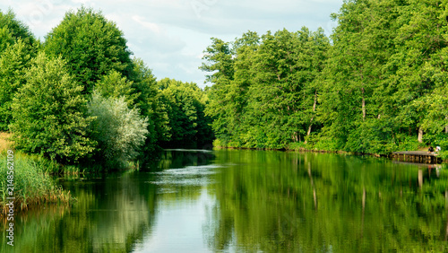 Obraz na plátne Calm river flows between green trees under blue sky in a quiet area The Augustow Canal on the Vistula River and the Neman River in Belarus Grodno Region on July 25, 2026