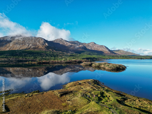 Aerial view of the rugged Connemara landscape with Twelve Bens mountains reflecting in a calm lake, green fields and rocky terrain, Municipal District of Conamara, County Galway, Ireland.