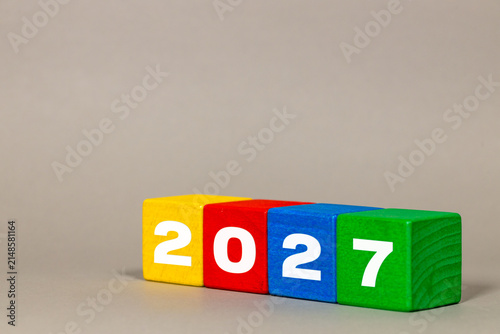Year 2027 written on colorful wooden toy blocks lined up in a row on grey background with large copy space for text, future planning and new year concept.